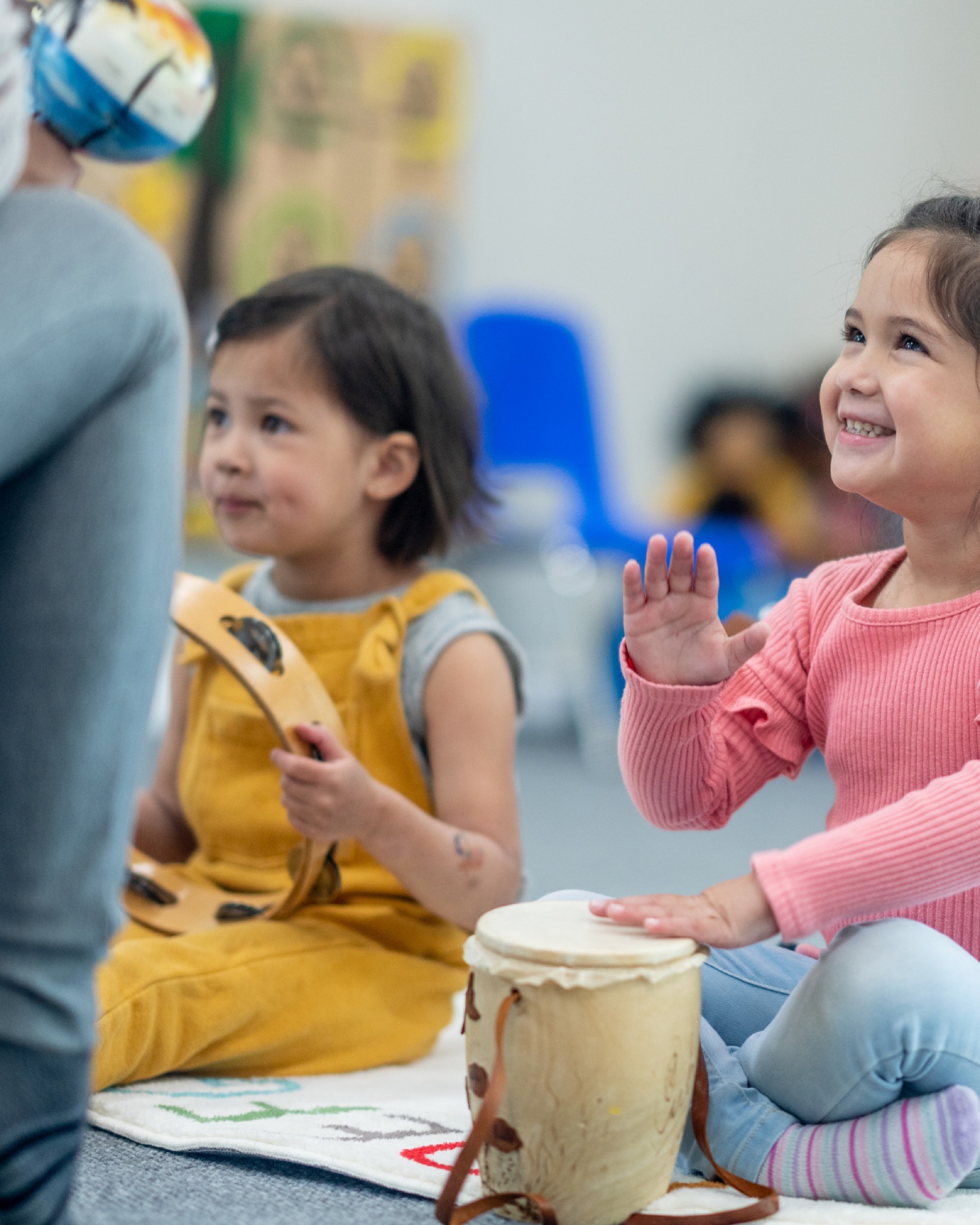 Two preschoolers playing tambourine and djembe in a Little Rockers daycare music circle
