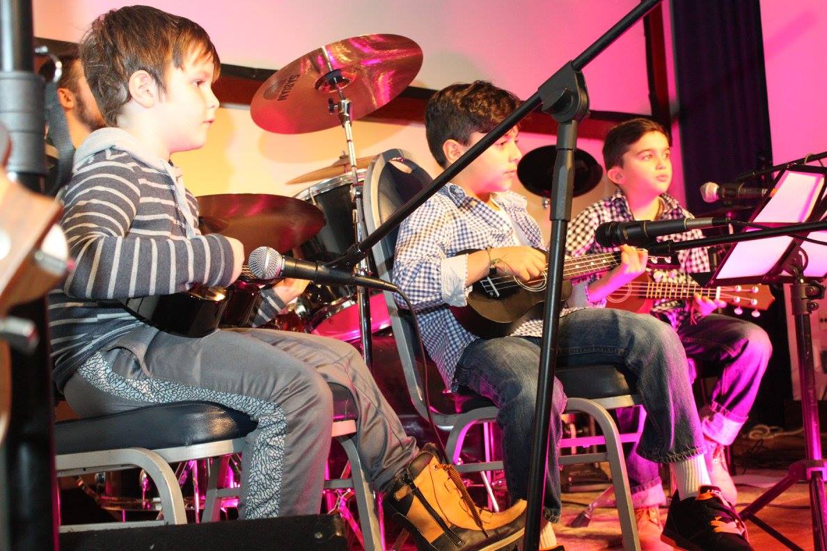 Students playing ukulele on stage with the band